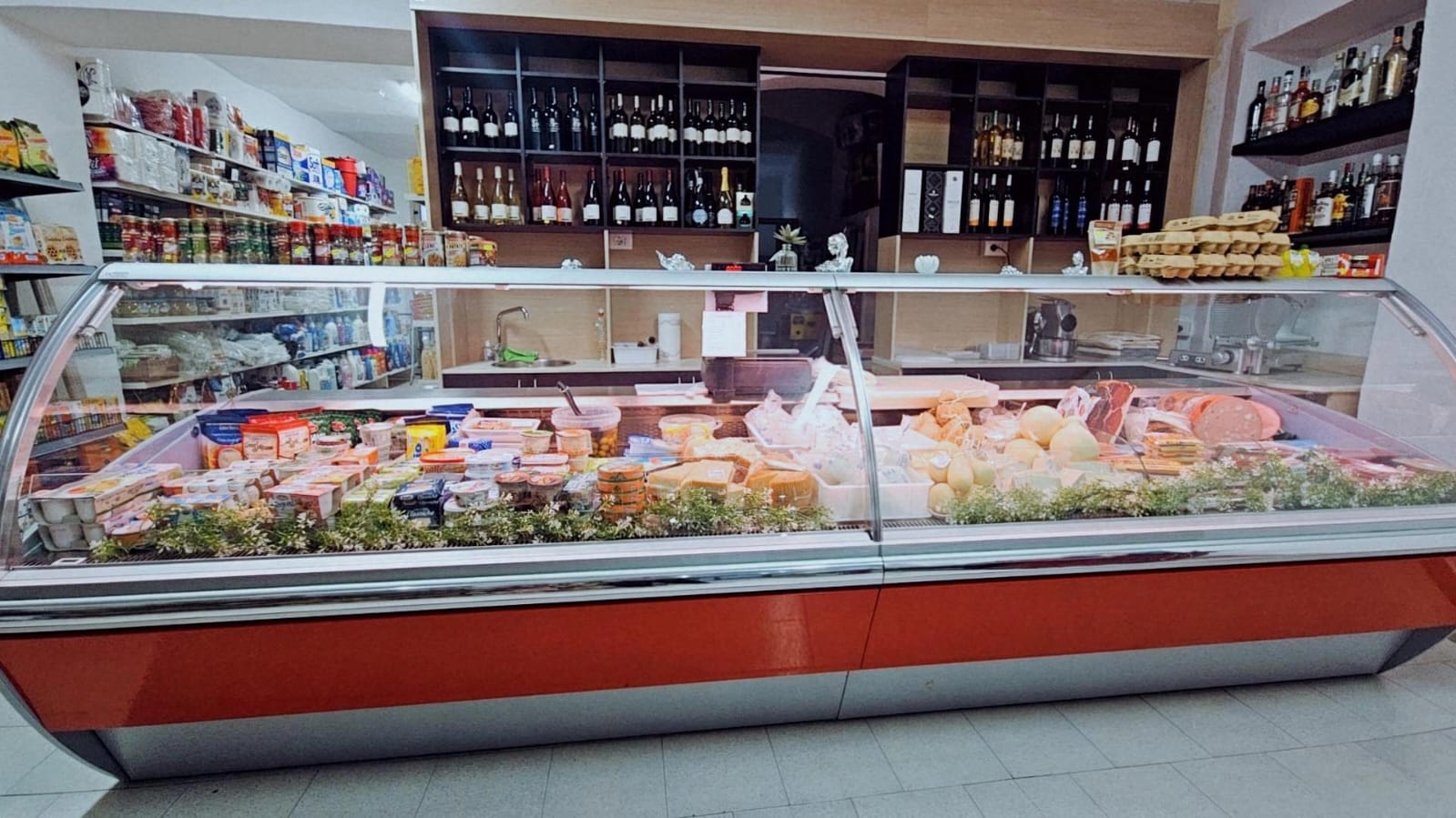 Banco frigo con salumi, formaggi e latticini, dietro gli scaffali dei vini